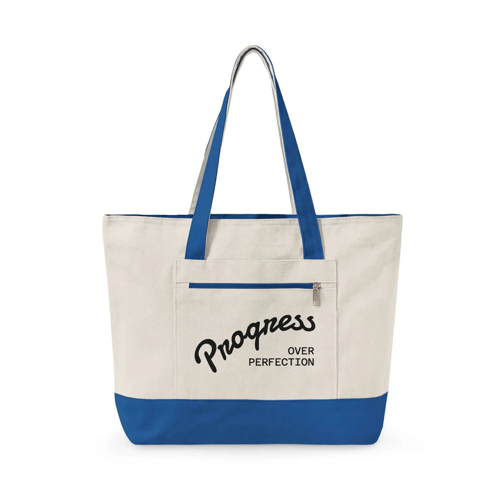 Progress Over Perfection Tote Bag | Minimalist canvas tote bag with black straps and zipper pocket featuring the motivational quote “Progress Over Perfection” in bold black typography on a neutral cream background.